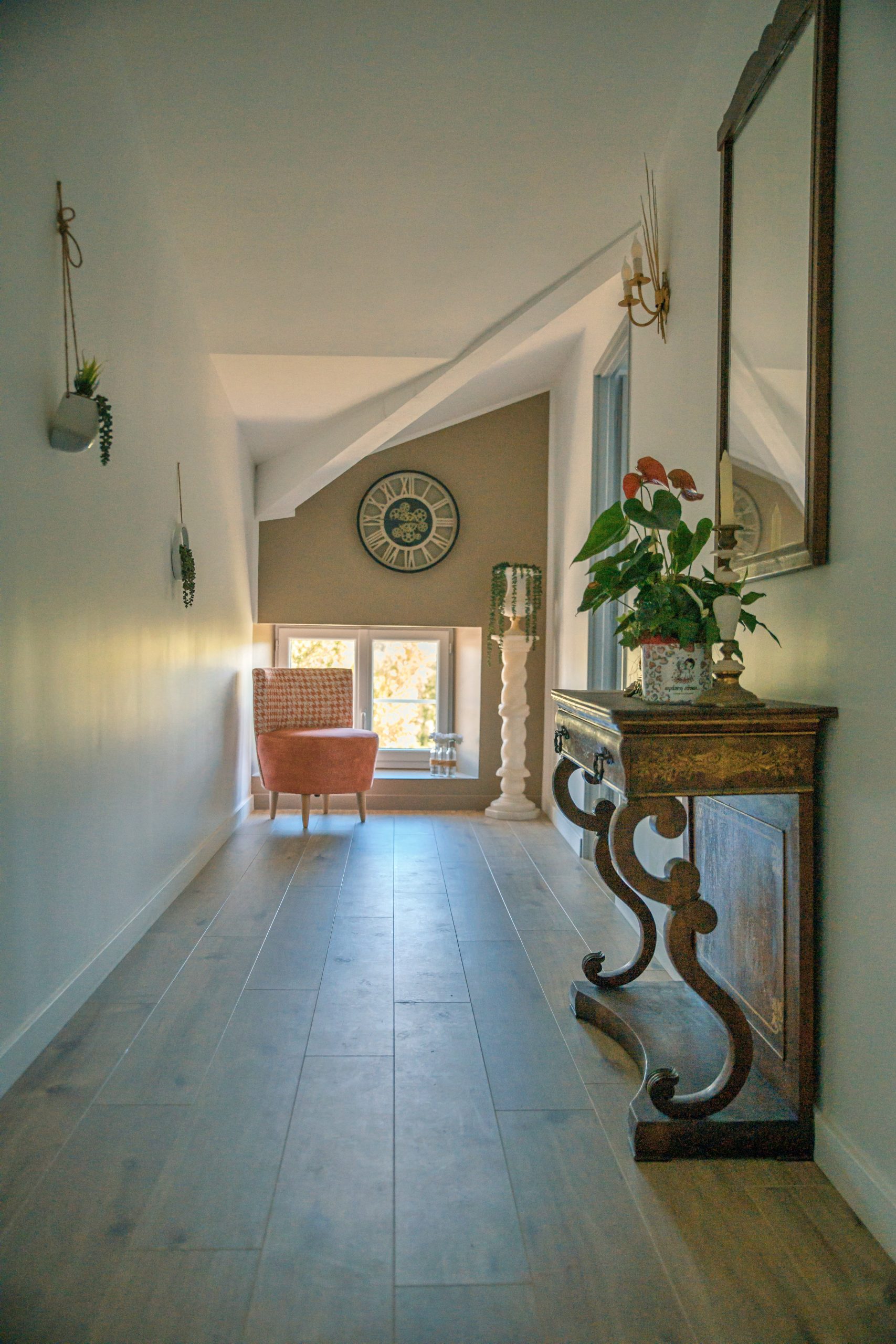 Vue du couloir principal élégamment décoré d’une maison d’hôtes de charme, avec un éclairage chaleureux, des œuvres d’art aux murs et des portes menant à des chambres luxueuses.